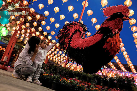 مادر و دختر نشسته در کنار یک مجسمه خروس در آستانه سال نو قمری - بانکوک، تایلند