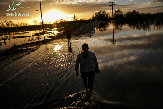 یک مادر و پسرش در حال عبور ا زیک جاده آب گرفته در گریدلی، کالیفرنیا