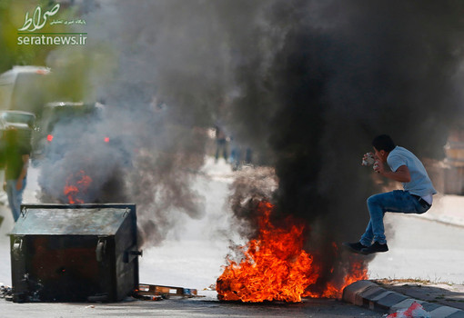 جوان فلسطینی با سنگهایی در دست در مقابل لاستیک آتش زده در تظاهرات بیت لحم