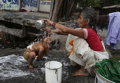 یک زن در حال شستن فرزند خود در کنار آب های آلوده - الله آباد، هند