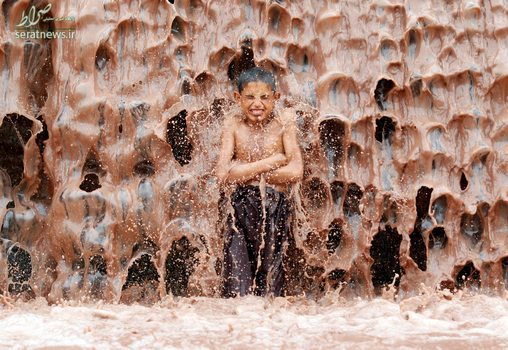 دوش گرفتن یک پسر بچه افغان زیر یک آبشار گل آلود