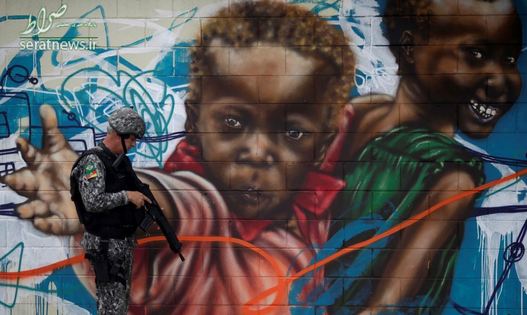 یک نیروی امنیتی برزیل ایستاده در مقابل یک دیوار نقاشی شده در محله ای فقیرنشین