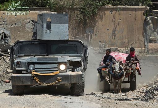 یک خودروی نظامی ارتش عراق در حال عبور از کنار دو پسر گاری سوار در غرب موصل