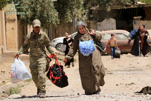 یکی از اعضای نیروهای واکنش سریع عراق در حال کمک به یک زن در موصل