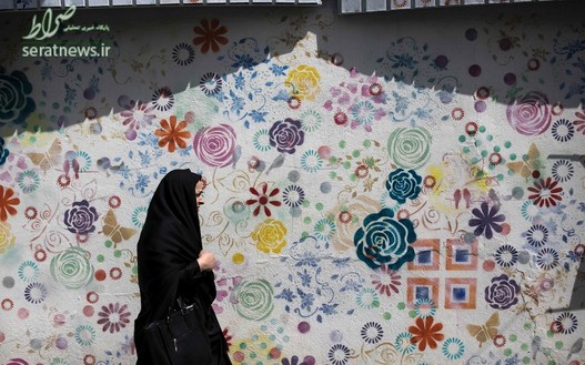 یک زن ایرانی در حال عبور از مقابل یک نقاشی دیواری در تهران