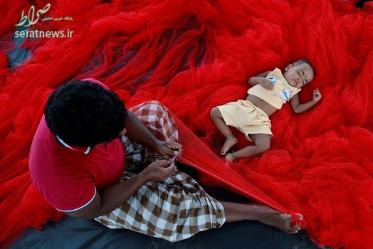 یک ماهیگیر در حال ترمیم تور ماهیگیری قرمز رنگ خود