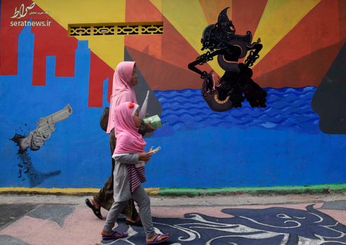 یک زن و دختر در حال عبور از کنار یک دیوار نقاشی شده در روستایی در اندونزی