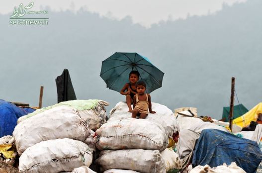 کودکان نشسته بر روی کیسه های پر شده از مواد قابل بازیافت در یک محل دفن زباله - گواهاتی، هند