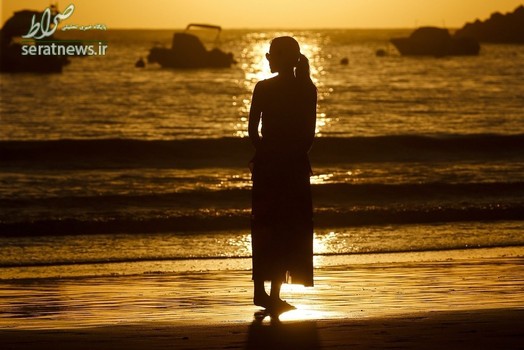 یک زن ایستاده هنگام غروب افتاب در ساحل سن سباستین لا کرنا در ایالت باسک، شمال اسپانیا