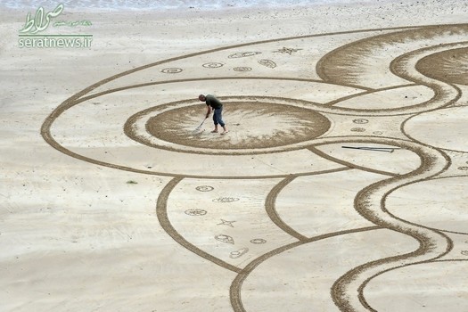 یک هنرمند در حال نقاشی بر روی شن و ماسه ساحل ولز