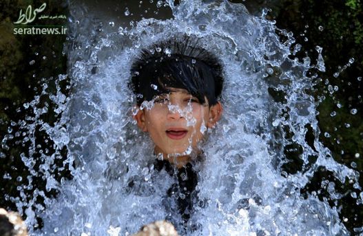 یک پسر نشسته زیر یک لوله آب برای خنک شدن در  هوای گرم پیشاور پاکستان