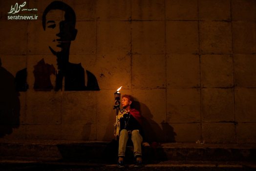 یک زن مشعل به دست نشسته در کنار یک نقاشی دیواری در کاراکاس