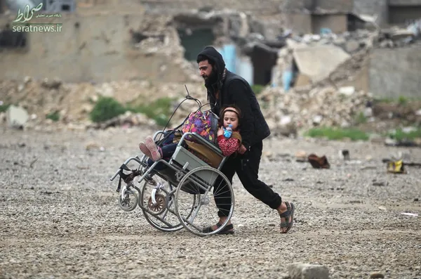 یک مرد عراقی در حال هل دادن ویلچر یک دختر در موصل