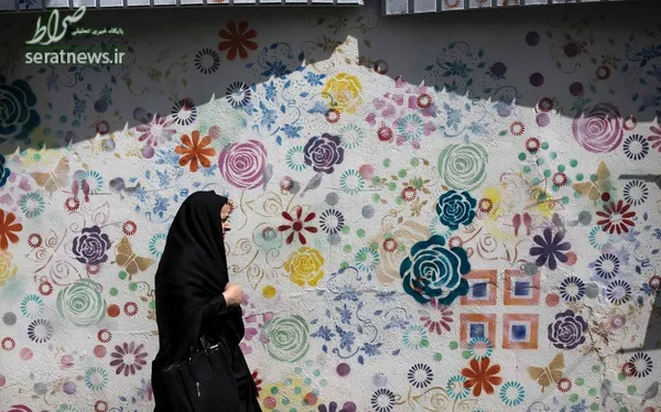 یک زن ایرانی در حال عبور از مقابل یک نقاشی دیواری در تهران