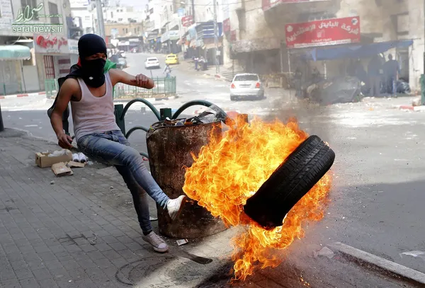 یک معترض فلسطینی در حال لگد زدن به یک لاستیک آتش زده در کرانه باختری